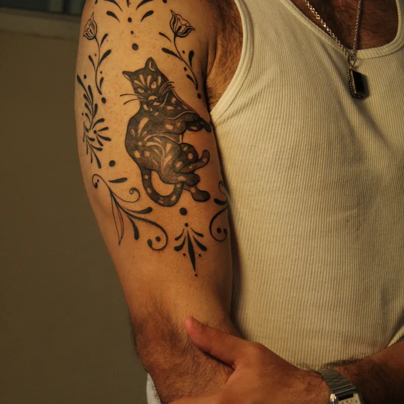 Silhouette cat framed by botanical vine leaves on upper arm